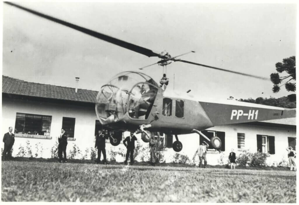  Uma fotografia em preto e branco mostra um helicóptero de pequeno porte com a matrícula "PP-H1